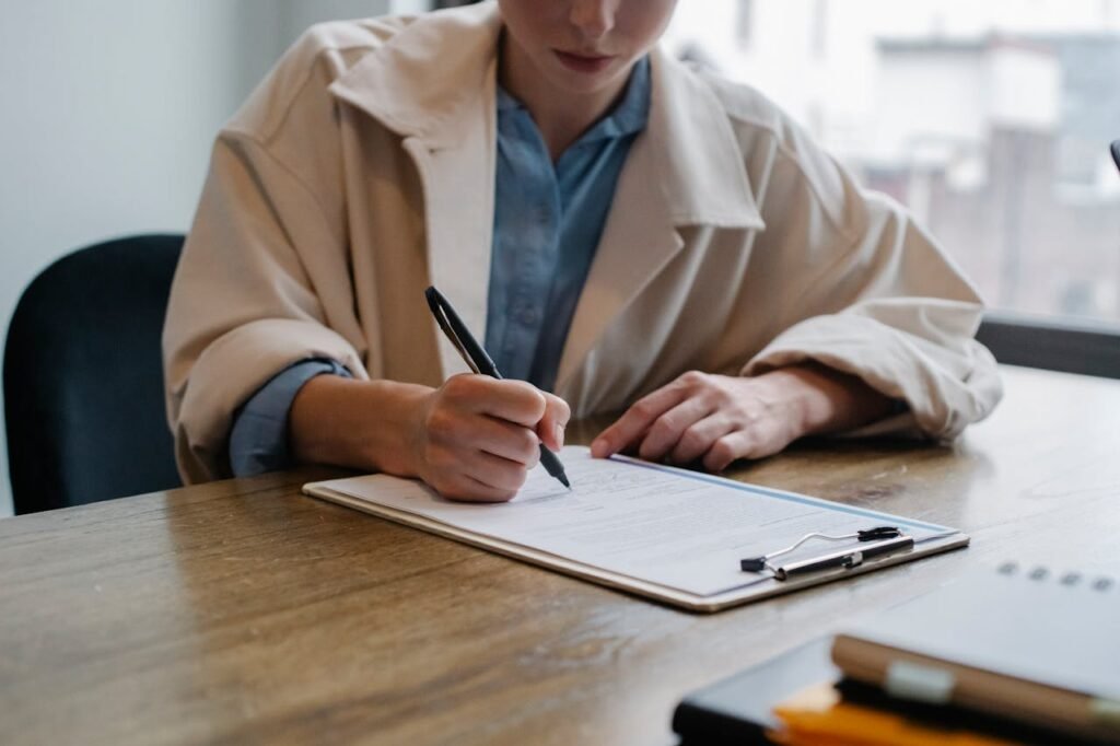 Crop young female unemployed job seeker filling questionnaire sitting at table during interview in office
